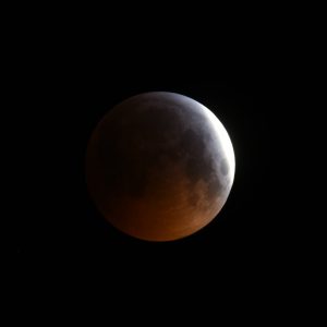 Teleskopaufnahme einer partiellen Mondfinsternis kurz vor Eintritt der Totalität. Ein Teil des Mondes oben rechts ist noch hell, auf der linken Seite wird bereits die kupferrote Farbe einer totalen Mondfinsternis sichtbar